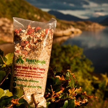 Close up of TentMeals Super seed and red berry breakfast sitting in a hedge, with mountains and a lake in the background.